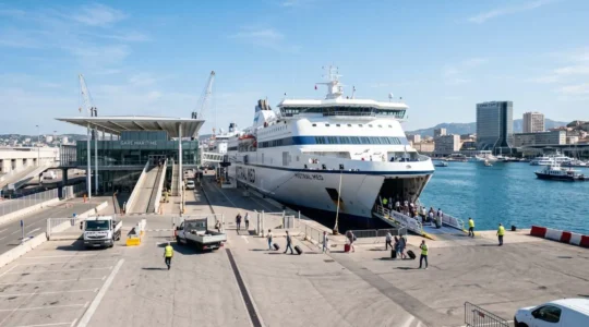 Un grand ferry blanc amarré le long d'un quai moderne dans un port méditerranéen sous un ciel bleu matinal